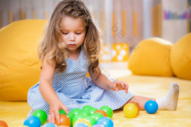可爱的白种孩子坐在地毯和演奏五颜六色的球在幼稚园