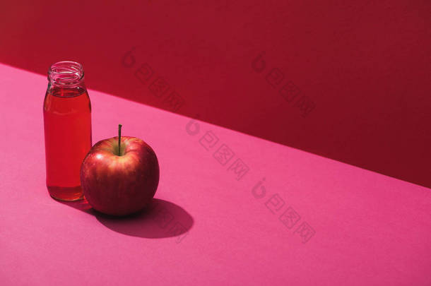 fresh juice in bottle near <strong>apple</strong> on red and pink background