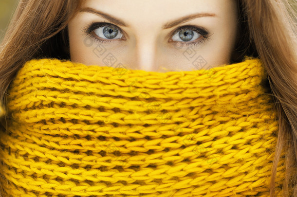 在一个黄色的针织围巾，看看相机的漂亮女人。可好看