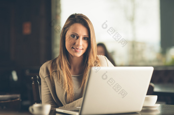美丽的女人，坐在咖啡馆里一台笔记本电脑