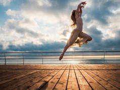日出时分跳芭蕾舞女演员在米色的衣服和普安特在路基之上大洋或大海的海滩上。美丽的金发女人锻炼伸展和经典的长头发。史诗般的跳转.