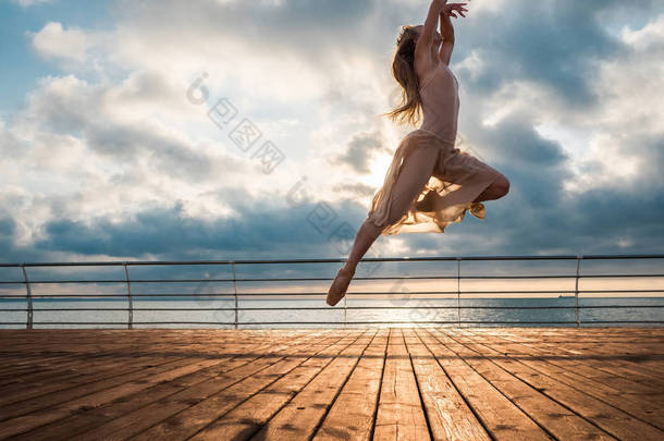 日出时分跳芭蕾舞女演员在米色的衣服和普安特在路基之上大洋或大海的海滩上。美丽的金发女人锻炼伸展和<strong>经典</strong>的长头发。史诗般的跳转.