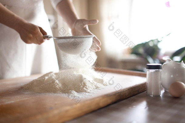 面粉筛入碗在厨房里的年轻女子