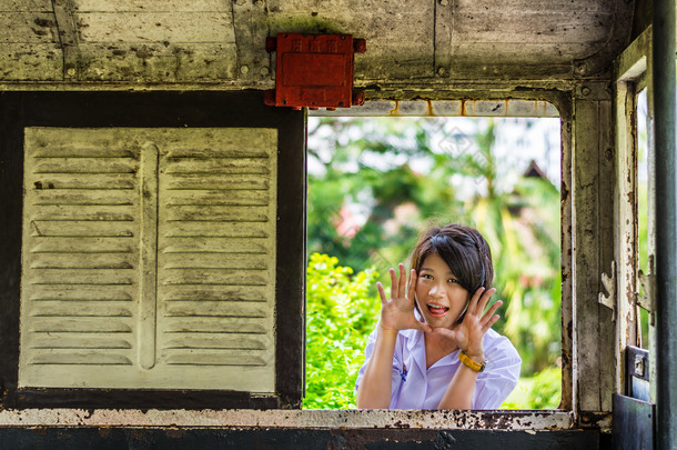 可爱的亚洲泰国女学生穿制服给一个<strong>惊喜</strong>呢通过旧复古窗口面板。没有人会将吓倒?