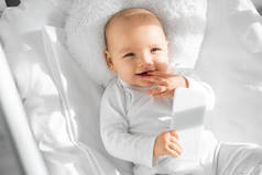愉快的婴儿抱着智能手机在白色婴儿床 