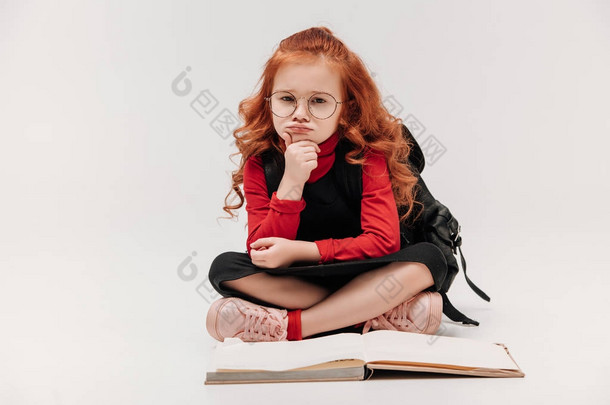 无聊的<strong>小女生</strong>坐在地板上与打开的书孤立灰色