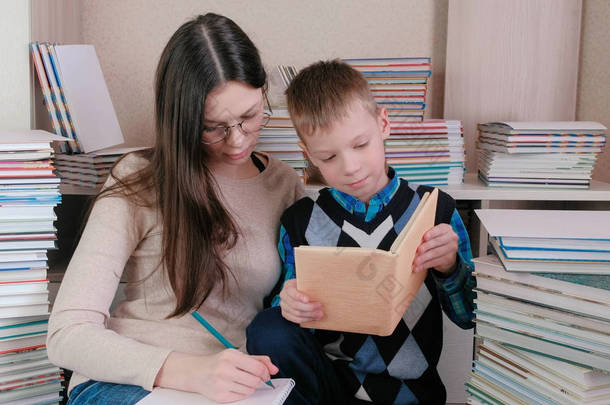 妈妈和儿子一起读了一本书。戴眼镜的妈妈在笔记本里写东西.