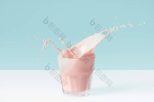 蓝色背景玻璃上溅出的草莓奶昔 