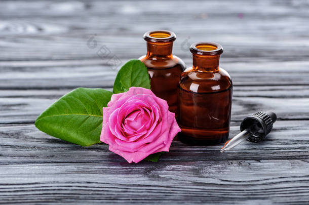 木质表面天然草本精油、吸管和粉红色玫瑰瓶