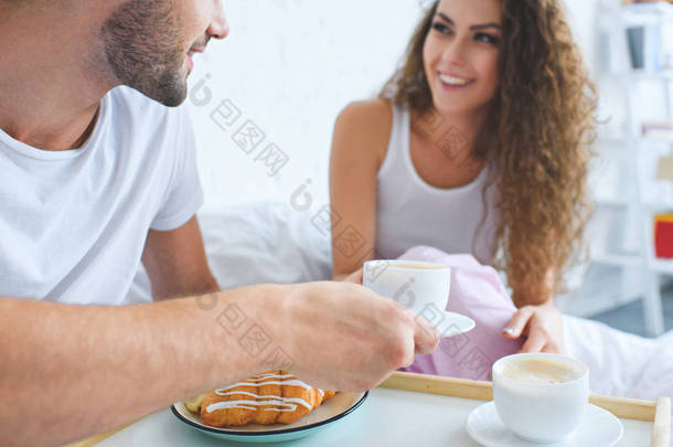 微笑的年轻夫妇在床上吃牛角面包和咖啡的镜头  