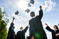 青年毕业学生在蓝天前投掷帽子的底层视角