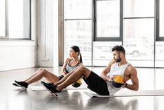 运动年轻夫妇在运动服装手持药丸和在健身房的瑜伽垫锻炼的侧视图