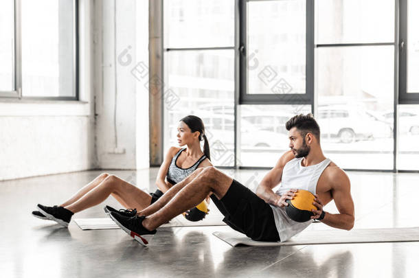 <strong>运动</strong>年轻夫妇在<strong>运动</strong>服装手持药丸和在健身房的瑜伽垫锻炼的侧视图