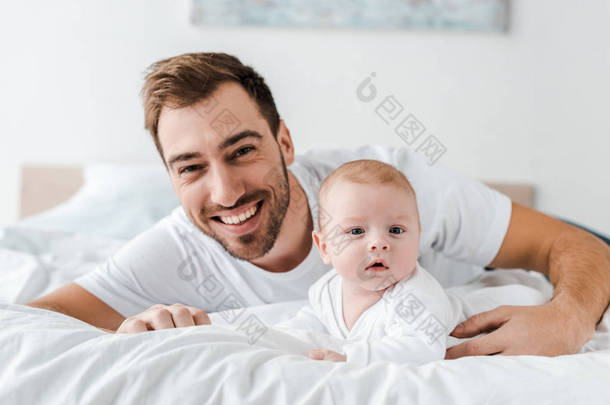 笑爸爸躺在床上可爱的婴儿，看着相机