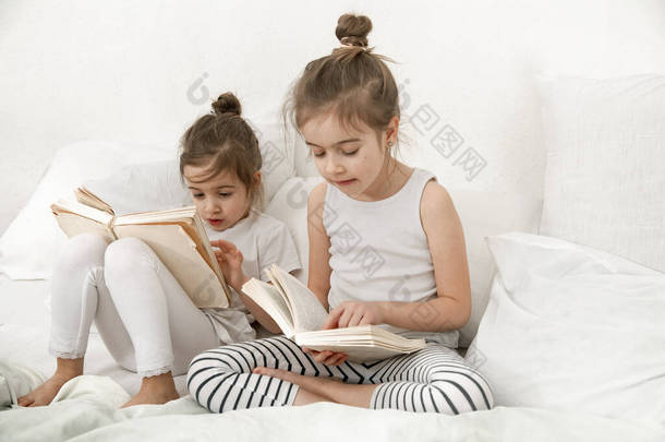 两个可爱的妹妹正在卧室的床上看书。家庭价值观和<strong>儿童</strong>友谊的概念.