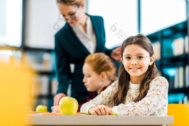 美丽的小学生微笑着在相机, 而学习与同学和老师在图书馆  