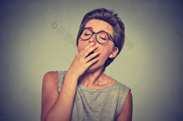 headshot sleepy young woman with hand over open mouth yawning