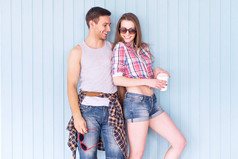 对幸福的夫妇朋友戴着太阳镜，夏季牛仔服装街城市休闲风格说话有好玩的站在墙附近