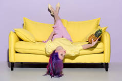 美丽的年轻女子躺在黄色的沙发上与菠萝