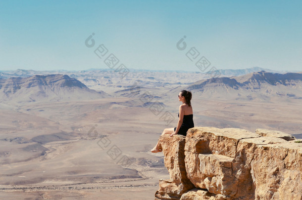 女孩看着沙漠景观的悬崖上