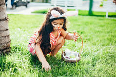 可爱的小女孩与兔子耳朵和复活节彩蛋篮子在花园里。寻找复活节彩蛋