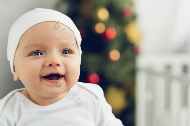 特写肖像的快乐小宝宝在白色的帽子与模糊的圣诞树背景