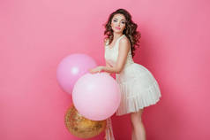 开朗美丽的年轻女孩穿着与闪闪发光的粉红色氦气球享受生日拍摄跳舞和微笑的粉红色背景可爱的女人摆在演播室。时尚生活方式情感