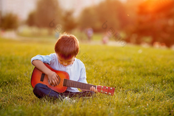 吉他，坐在草地上<strong>的</strong>可爱男孩