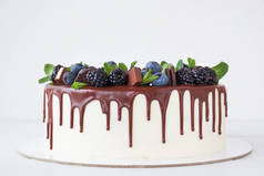 蛋糕与巧克力, 装饰着后浆果, 蓝莓, 薄荷叶, 巧克力棒和饼干在白色的桌子上.