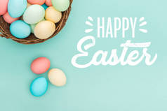 柳条篮中五颜六色的彩蛋的顶视图，蓝色背景上的白色快乐复活节字母