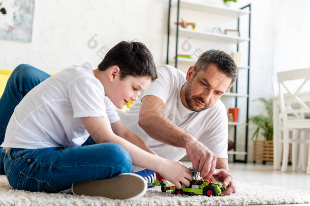 父亲和儿子坐在地毯上玩玩具车在家里的客厅