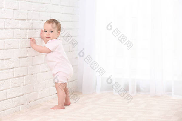 可爱的婴儿抱着墙在室内。学习走路