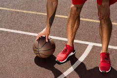 在篮球场上穿着红色运动鞋与球的运动员的裁剪视图