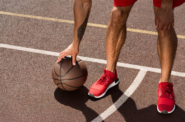 在篮球场上穿着红色运动鞋与球的运动员的裁剪视图