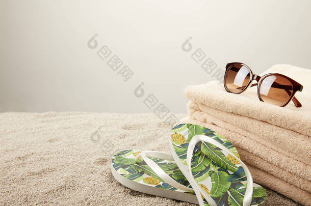 在灰色背景下, 对<strong>沙滩</strong>上的毛巾、太阳镜和<strong>夏季</strong>翻转的拖鞋进行特写查看