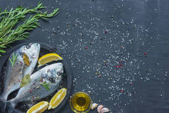 从上面的生鱼与柠檬, 月桂叶和迷迭香在托盘上的黑色表覆盖着盐和胡椒
