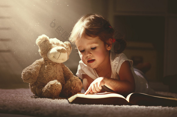 孩子读一本魔法书在黑暗的家中的小女孩 