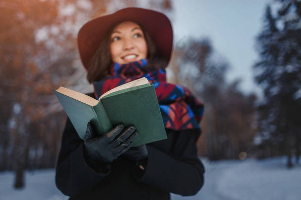 红色帽子持有和阅读诗歌书在冬季森林背景的年轻女子