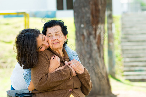 站在祖母拥抱和拥抱在户外环境中后面的年轻女孩