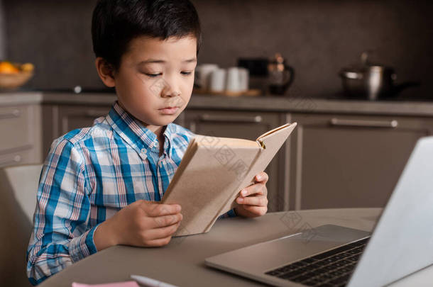 <strong>在</strong>自我隔离期间，亚洲男孩<strong>在</strong>家里看书，带着笔记本电脑上网学习