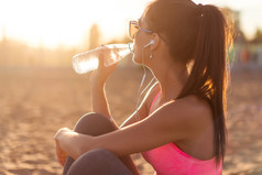 户外锻炼在傍晚夕阳夏天在海滩室外肖像上下班后美丽健身运动员女人喝水.