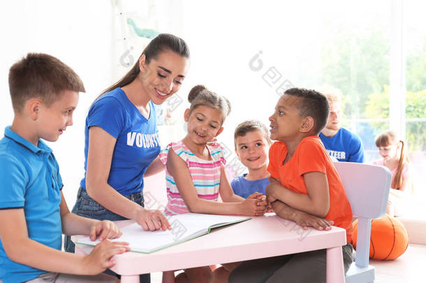 青年志愿者在室内餐桌上与儿童一起阅读书籍