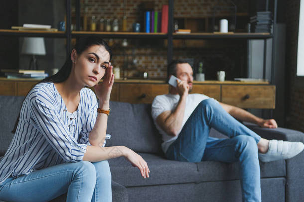 <strong>郁闷的女人</strong>坐在沙发上, 而她<strong>的</strong>丈夫电话聊天模糊背景