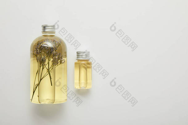 透明瓶的顶视图与天然液体黄色美容产品与草药在灰色背景 