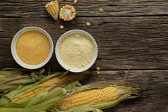 把玉米粉和玉米粉放在木制桌子上的瓷碗里. 玉米的耳朵和玉米的碎片旁边碗。 无麸质健康饮食