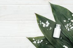 在绿色棕榈叶上的瓶中,椰子美容产品顶视图,白色木表面有椰子片