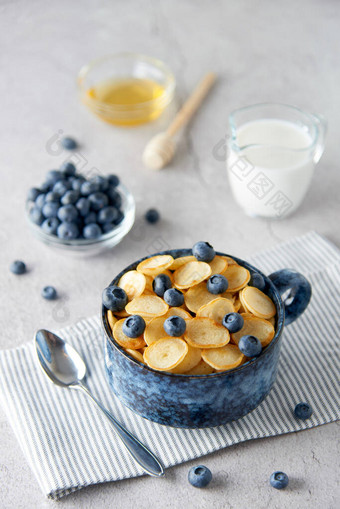 蓝色碗的迷你煎饼麦片与蓝莓，枫糖浆和牛奶的混凝土背景。小煎饼，新的食品潮流概念。美味的健康早餐或小吃。食谱、菜单.图片