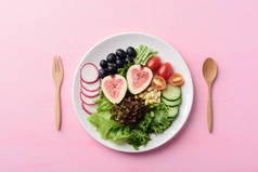 色拉，盘子里有水果和蔬菜，有木叉和勺子，粉红的面糊背景，健康的素食，俯瞰