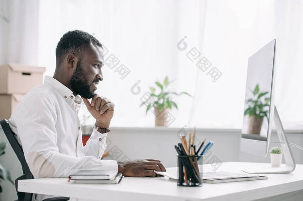 一个快乐英俊的非洲裔美国商人在办公室的电脑前工作的侧视图