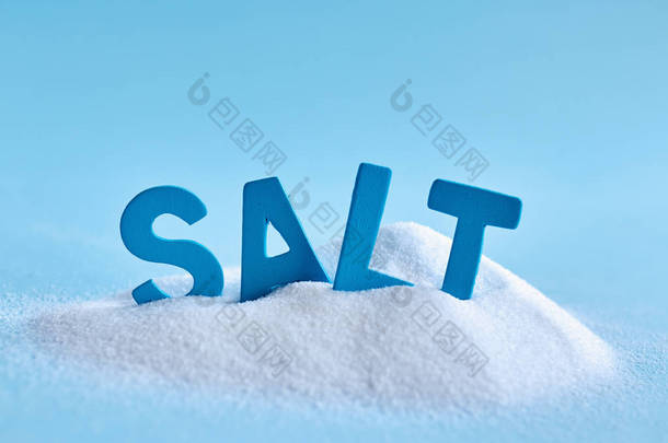 溢出的盐和蓝色字母的特写照片在蓝色背景上拼写单词盐